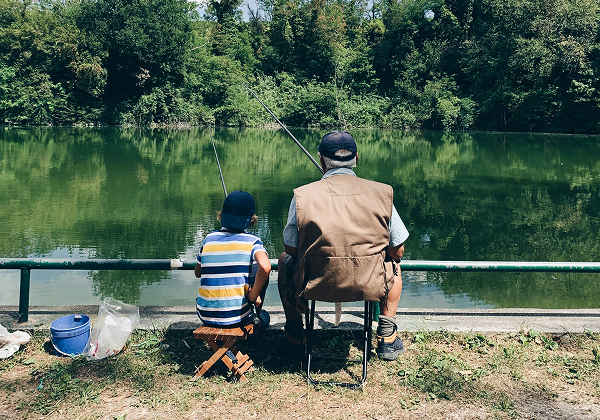 Ein Kind und ein Erwachsener sitzen mit ihren Angeln an einem idyllischen See.